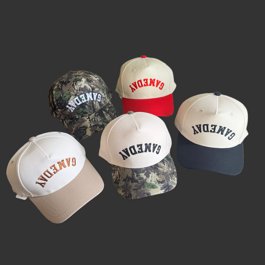 Five caps with 'GAMEDAY' embroidered in various colors and patterns on a cream background