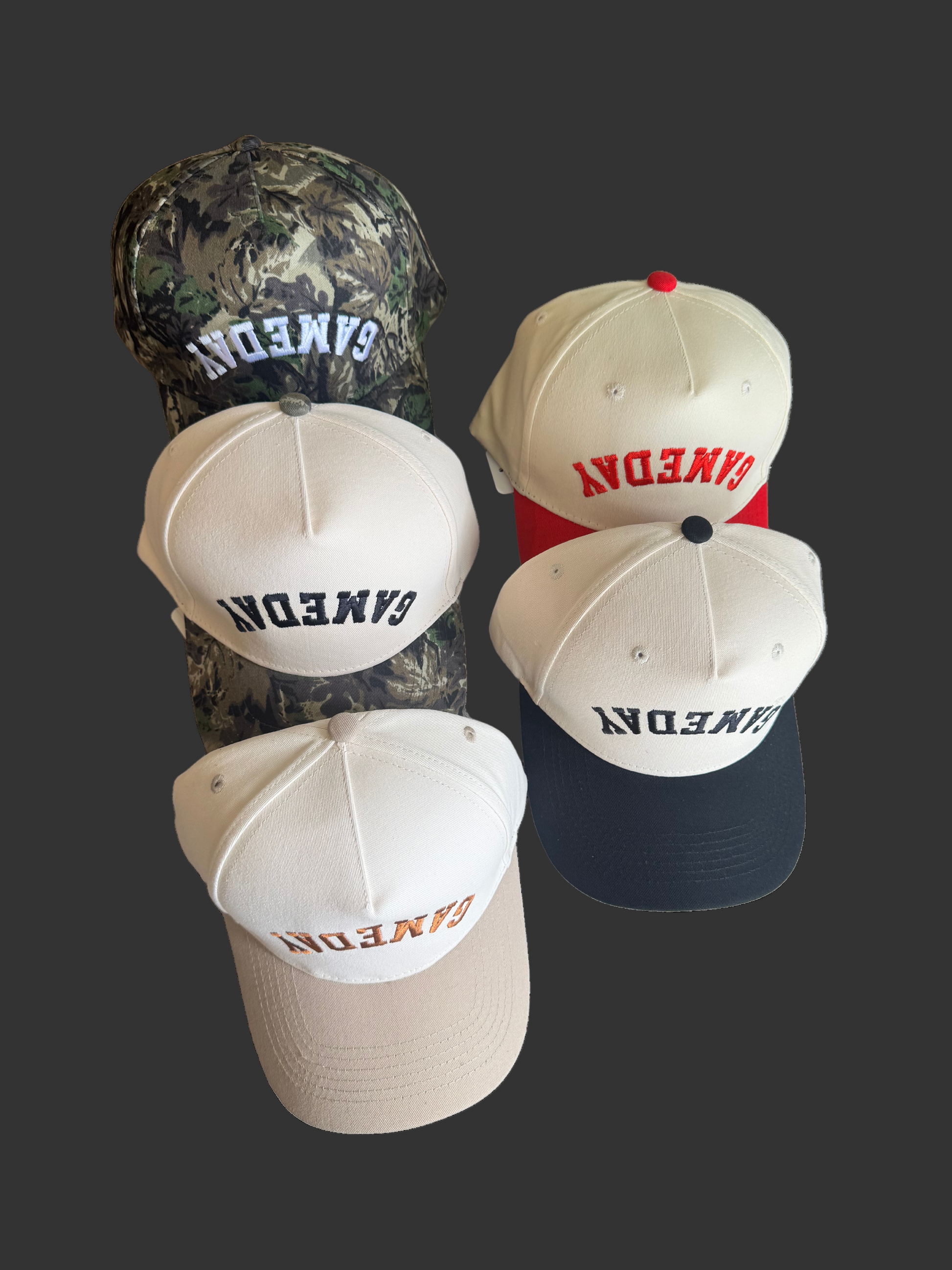 Five baseball caps with 'GAMEDAY' embroidered upside down in various colors on a cream background